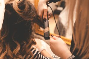 Hairdresser makes hair styling with curling iron